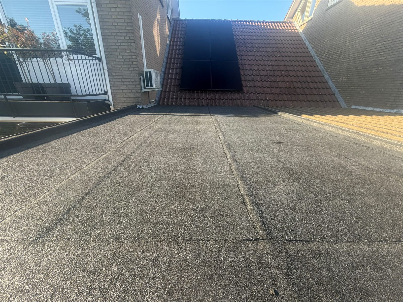 Afgewerkt bitumen dak van een aanbouw bij een pannendak met zonnepanelen