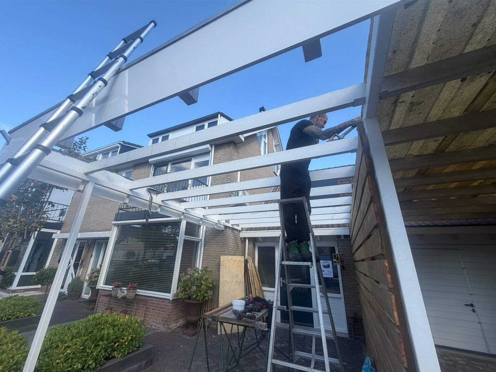 Dakdekker werkt op een ladder aan een houten terrasoverkapping