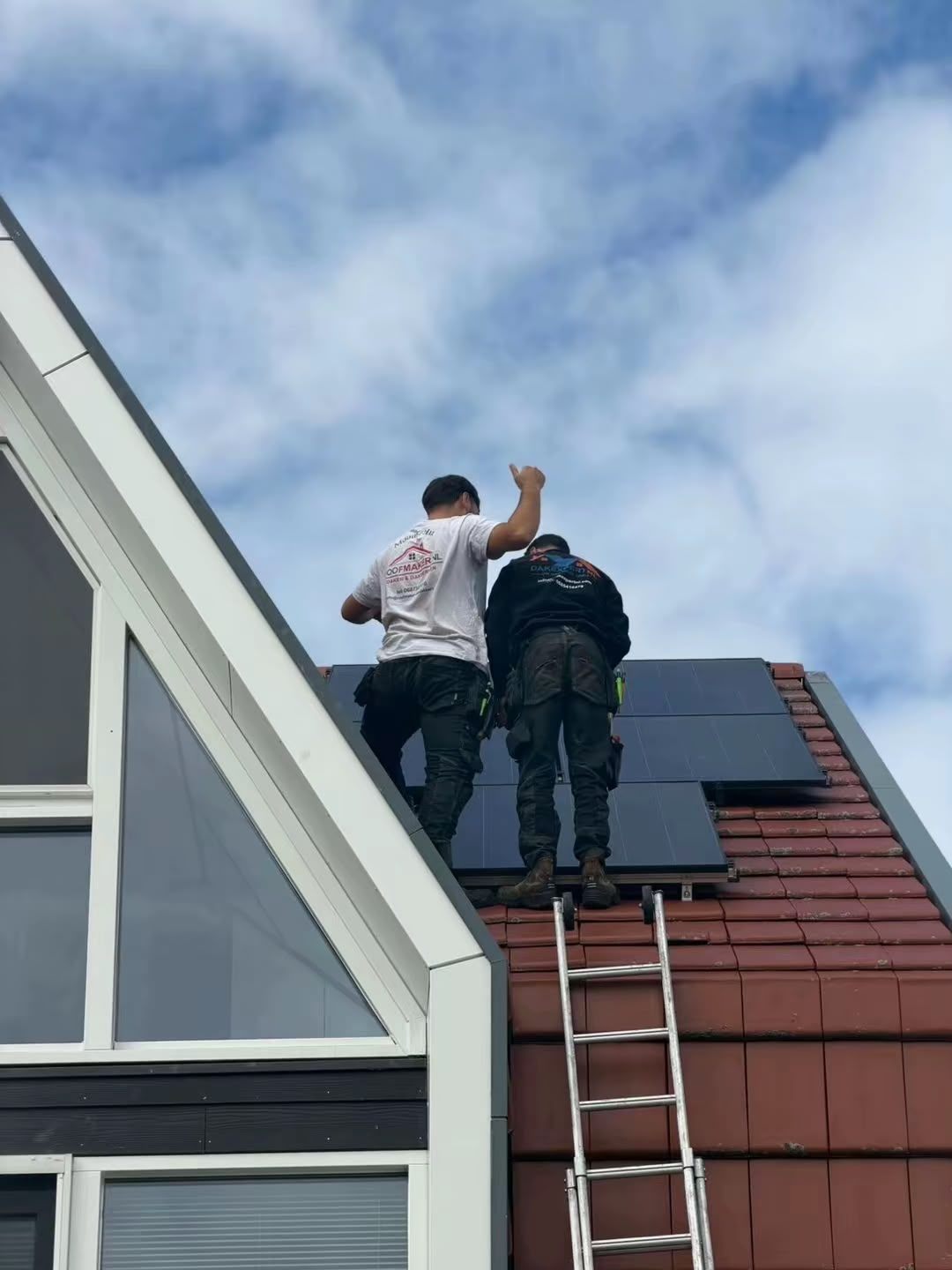 Dakdekkers aan het werk op een rood pannendak met zonnepanelen